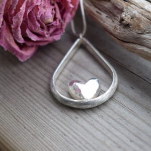 droppformat silverhalsband med hjärta i mitten på trä med en ros bredvid utomhus