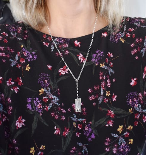 andashalsarm3-2.jpg kvinna med blommig blus med silverhalsband med texten ANDAS