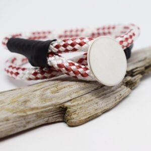 rödvitt armband med silverbricka på träbit