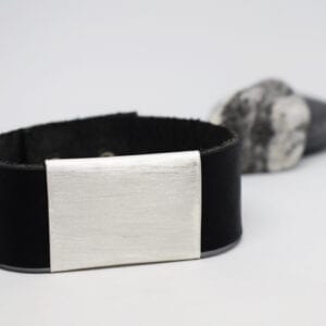 läderarmband med silverbricka på vit botten med sten i bakgrunden