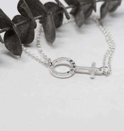 litetgirlpwerarmband2 kvinnomärket som armband i silver mot vit bakrund med en grun kvist liggandes bredvid