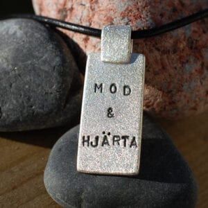 borstad silverbricka med text i läderrem på stenar utomhus i