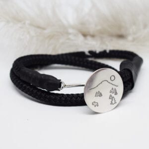 svart armband med silverbricka på vit botten med fjäder i bakgrunden