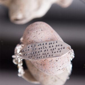 armband i silver med lång text på rosa sten som ligger på en spegel