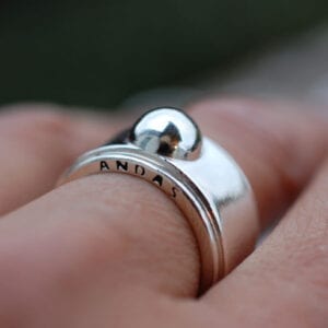 bred silverring med texten ANDAS på kanten på finger utomhus