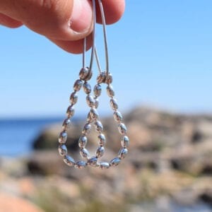 droppfromade silverörhängen som hålls i en fingernypa ute vid havet