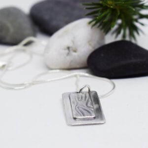 silverhalsband med mönster med stenar och grankvist bakom