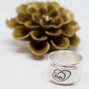 Bred silverring med tassar på mot vit bakgrund och blomma