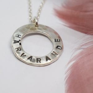 silverhalsband med text på vit botten med rosafjäder bredvid