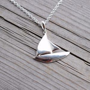 silverhalsband i form av en segelbåt på trä utomhus